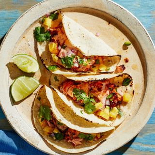 Three salmon tacos on a plate topped with pineapple salsa and served with lime wedges for squeezing.