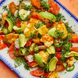 A citrus Halloumi and Avocado on a white and blue plate placed on a pink pastel surface