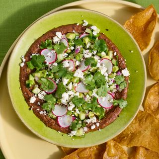 Cucumber and avocado salad bean dip on a platter shared with broken tortilla chips.