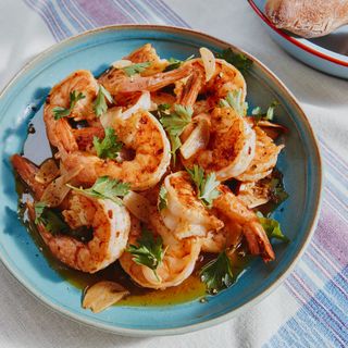 A bowl of shrimp sprinkled with parsley and chopped garlic with pieces of bread around it.